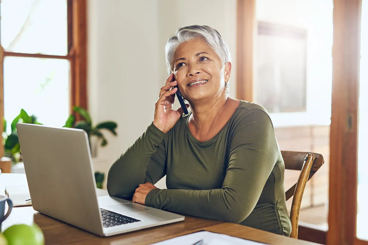An older woman smiling on the phone at her laptop